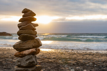 Fototapeta na wymiar Close up of a Stack of Stones Balance on a Beach Against a Cloudy Sky at Sunset Time.Zen Concept