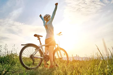 Foto op Canvas Cyclist Woman riding bike in helmets go in sports outdoors on sunny day a mountain in the forest. Silhouette female at sunset. Fresh air. Health care, authenticity, sense of balance and calmness.  © Andrii IURLOV
