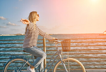 Carefree woman with bike riding on beach having fun, on the seaside promenade on a summer day....