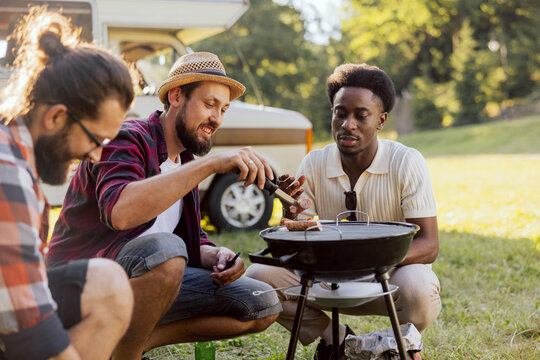 A Bearded Middle-aged Guy Is Preparing A Barbecue For Friends. A Group Of College Guys Hang Out Together. RV Trip