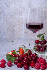 Appetizing, fresh, juicy, ripe grape, strawberry and raspberry assortment on light gray background. Red wine in glass in background.
