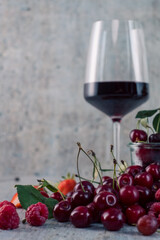 Appetizing, fresh, juicy, ripe grape, strawberry and raspberry assortment on light gray background. Red wine in glass in background.