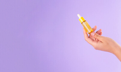 Serum bottle in female hands, top view. Yellow moisturizer for skin care. Nourishing essential oil in glass bottle with pipette. Liquid emulsion with hyaluronic acid. Beauty cosmetic spa product