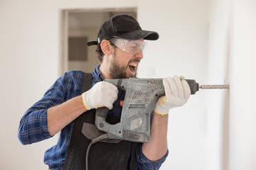Portrait of a young man with an electric drill and making a hole in the wall. Interior design and home renovation concept.