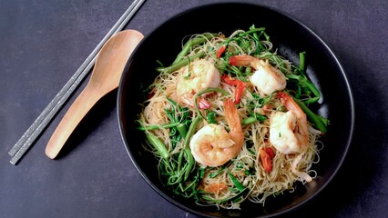Stir fried rice noodle with shrimp and water minosa vegetable or Mee Phat Krachet Koong in Thai on black background.