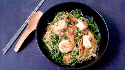 Stir fried rice noodle with shrimp and water minosa vegetable or Mee Phat Krachet Koong in Thai on black background.