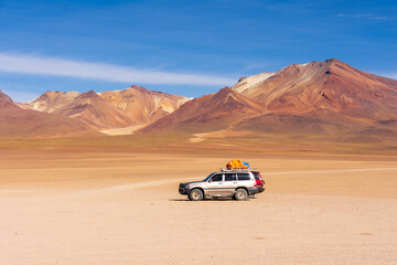 Two 4x4 cars wait in the Siloli desert with the colourful Andes in the background in the Altiplano...