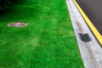 gray gutter of a stormwater system on the side of asphalt road with yellow markings and manhole in...
