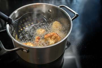 Deep frying cauliflower florets in a pot with boiling cooking oil on the stove, preparation of a...