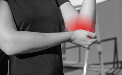 Athlete elbow pain, sports trauma. Woman holding painful arm with red point. Extensive training consequences. Health problems concept. Black and white. High quality photo