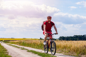 cyclist in red t-shirt and shorts riding a bike in the countryside. man cycling in summer.