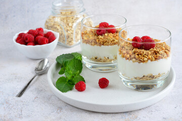 muesli with greek yoghurt decorated with raspberries and mint in drinking glasses on white tray