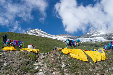 Snow suit are drying up in the valley with the snow capped mountains in the backdrop. Blue skies with few clouds over mountains and high altitude green meadow can be seen with drying snowsuits.