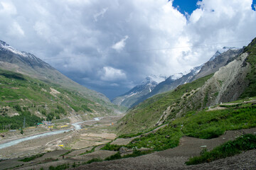 View of majestic mountains and greenery of step farms along with flowing chandra river through the entire lahaul valley. Snow covered peaks covered in dark clouds during monsoon season in India.