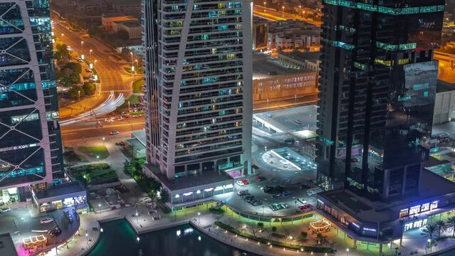Tall residential buildings at JLT district aerial night timelapse, part of the Dubai multi commodities centre mixed-use district. Parking on intersection and car parking