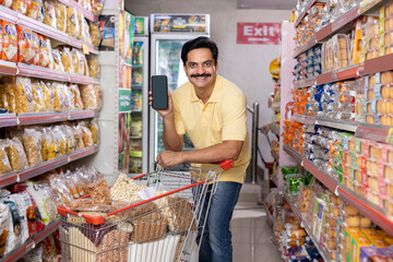 Happy man showing blank screen of mobile phone at grocery store