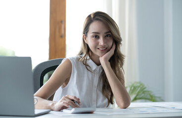 Charming Asian woman working at the office using a laptop Looking at the camera.