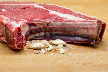 T-bone steak with garlic cloves and coarse salt on a wooden board. Veal. tender garlic Food and salting.