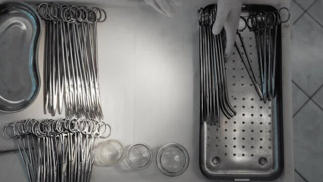 Close-up top view slow motion, scrub nurse in rubber gloves preparing surgical instruments placed on white table drape, healthcare worker prepares tools for surgery operation, hospital operating room.