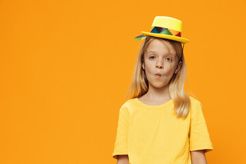 a cute, funny girl, of school age, stands on a yellow background in a yellow T-shirt in a straw hat. Horizontal studio photography with blank space for advertising mockup