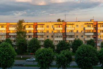 Fototapeta na wymiar Panel residential building surrounded by greenery and trees. A green city in an ecologically clean area. The house is flooded with the orange light of the setting sun
