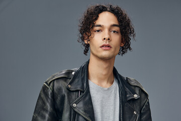 Obraz premium Pretty sexy self-confident stylish tanned curly man leather jacket posing isolated on over gray studio background. Cool fashion offer. Huge Seasonal Sale New Collection concept. Copy space for ad