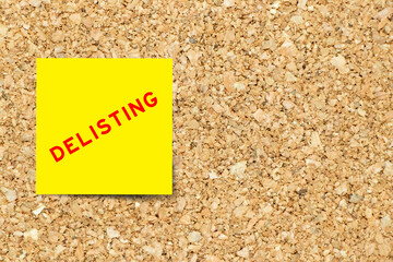 Yellow note paper with word delisting on cork board background with copy space