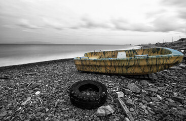 Black and white lanscape on a stony beach with used tyre on stones and yellow painted abandoned...