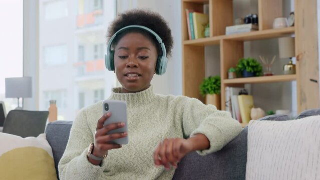 Listening to music from a phone on headphones, enjoying and nodding head from increased serotonin in home living room. Relaxed woman sitting on sofa, singing and browsing song playlist on technology