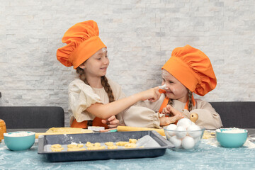 Happy family. Funny girls kids in orange chef uniform are preparing the dough, bake cookies in the kitchen. Sisters children enjoy cooking food. Warm relations.