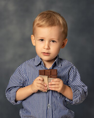 Portrait of small boy kid eating chocolate on grey background. Happy childhood concept. Sweet tooth.