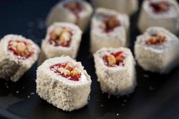 Turkish delight with strawberry jam, nuts and coconut flakes on a black plate