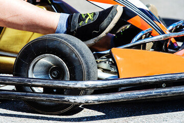 Fragment of a go-kart with a front wheel and a chrome bumper. Racer's foot on the gas pedal. Close-up