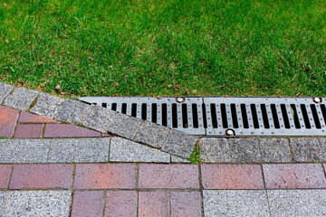 drainage grate bolted to storm drain at corner of pavement walkway path made of stone brick tiles...