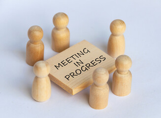 Wooden people figures having business meeting with meeting in progress text on wooden table.
