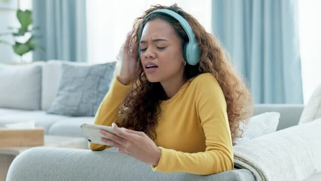 Confused and upset woman using phone and getting irritated with slow internet or wifi connection at home. Girl with headphones getting frustrated with losing mobile game or crashing streaming service