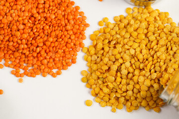 a tall glass jar with dry red and yellow lentils tipped on the white table and a measuring cup with lentils