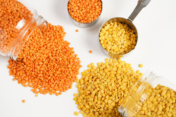 a tall glass jar with dry red and yellow lentils tipped on the white table and a measuring cup with lentils