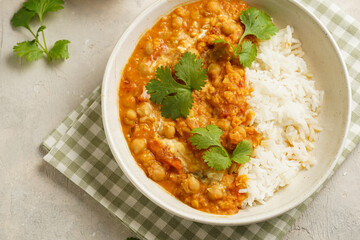 Indian red lentil curry with chickpeas, white rice and fresh cilantro - chana dal - in a white bowl on a green checkered kitchen towel