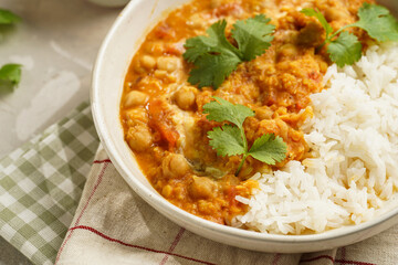 Indian red lentil curry with chickpeas, white rice and fresh cilantro - chana dal - in a white bowl on a green checkered kitchen towel