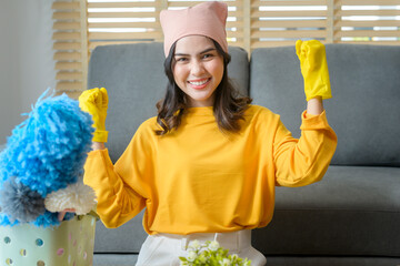 Young happy woman wearing yellow gloves  and holding a basket of cleaning supplies in living room.