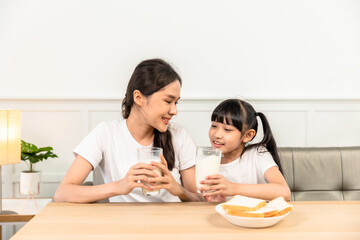 Asian  family enjoying breakfast at living room. little girl daughter sitting on table, drinking milk with smiling father and mother in morning. Happy family at home.