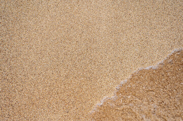 Feinkörniger Sand an einem Strand mit Wasser einer Welle als Textur mit Freiraum für individuelle Anpassungen