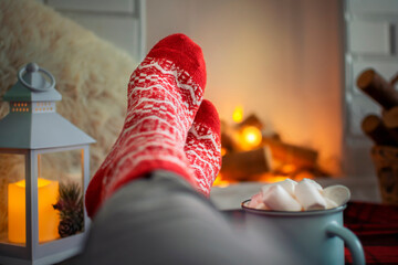 Cozy winter evening at home, feet in warm woolen red socks by the fireplace, a woman is relaxing...