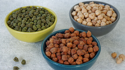Assortment of dry chickpea piles in bowls. Three different chick pea kinds: green, kala chana and white.