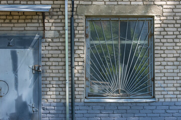 Close-up of the facade of an old brick building with a barred window and a metal door