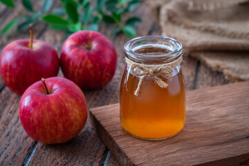 Apple cider vinegar in glass bottle and fresh red apples on wooden table
