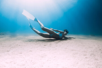 Freediver underwater glides with white fins. Attractive lady free diver in ocean with sun rays and sandy bottom