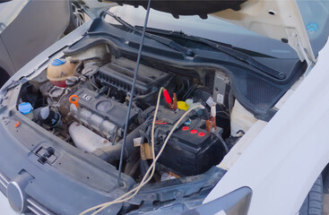 A car with an open hood. Charging the battery