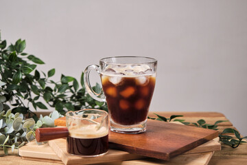 cold iced black brew coffee in a glass with pieces of ice on a wooden table, natural light, fresh summer drink in the morning
